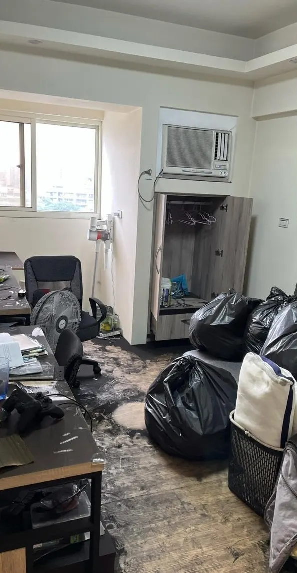 清潔前的房間,地板覆蓋大片黑色污漬並堆滿垃圾袋