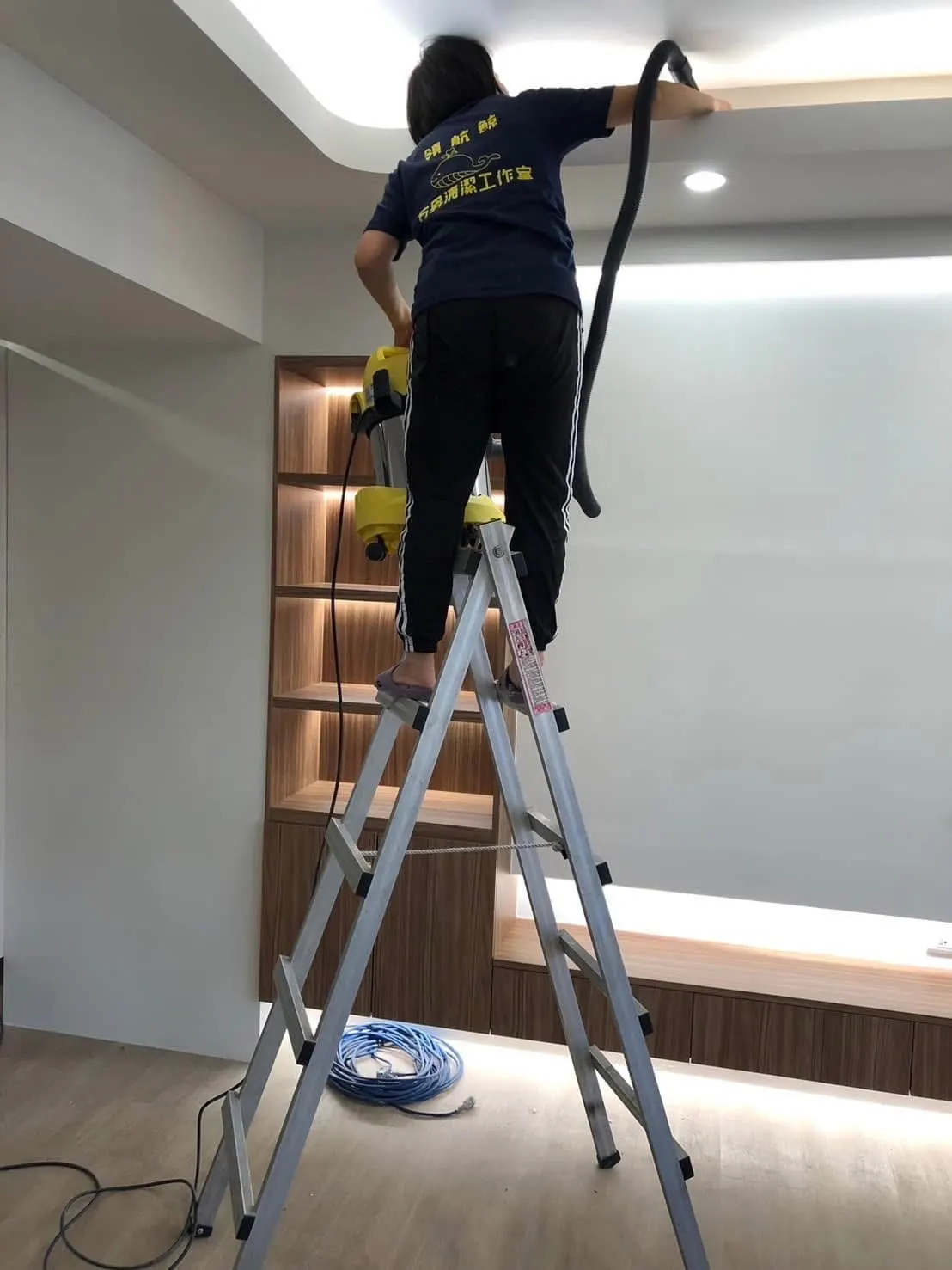 清潔人員站在梯子上,用吸塵設備清潔天花板間接照明的溝槽